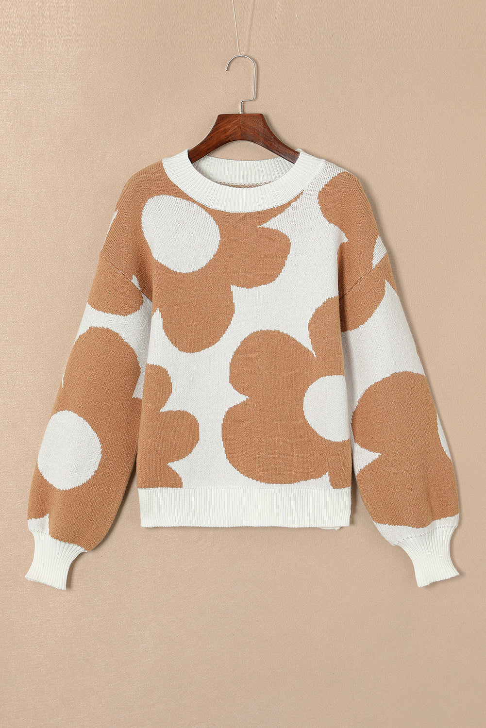 Brown and white patterned sweater on a hanger against a beige background